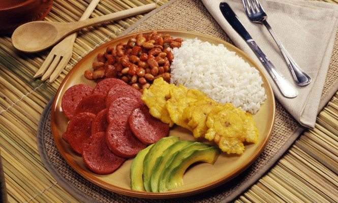 A typical Dominican plate with rice, beans, fried salami, avocado, and tostones (fried plantains).